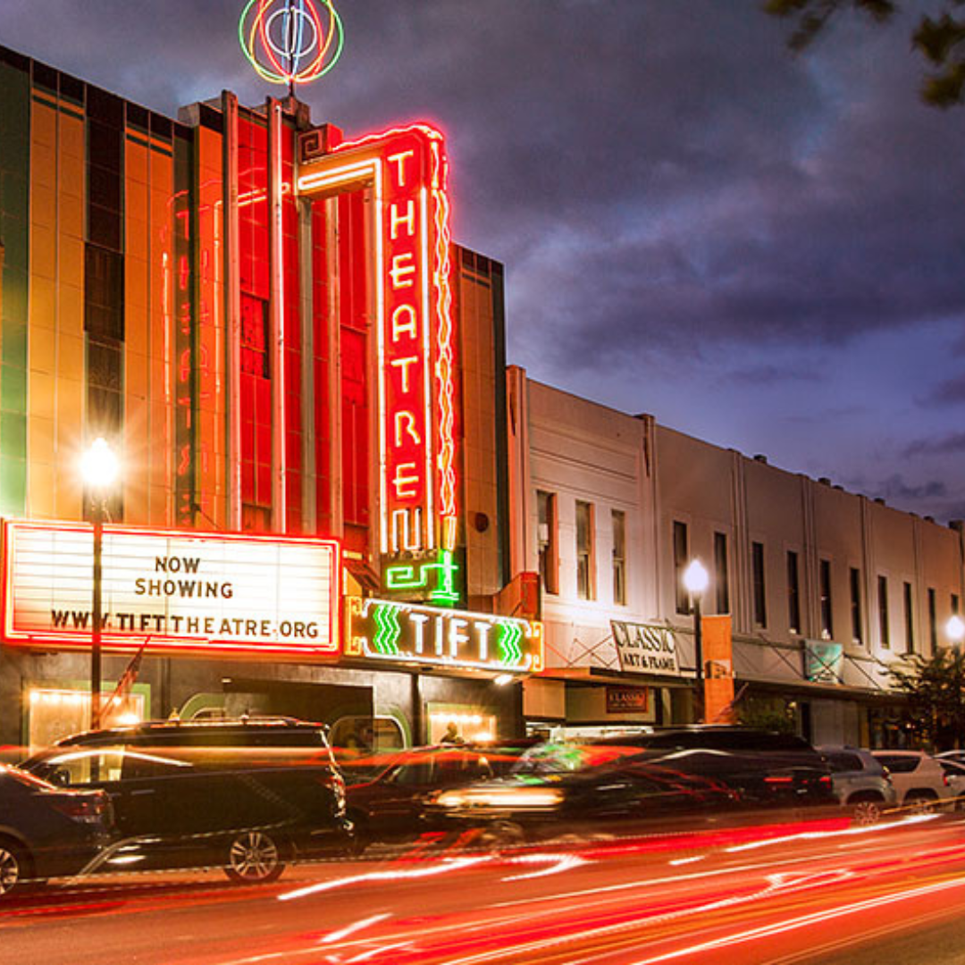 Evening view of the illuminated theater in downtown Tifton, GA, with glowing lights and a bustling street scene.